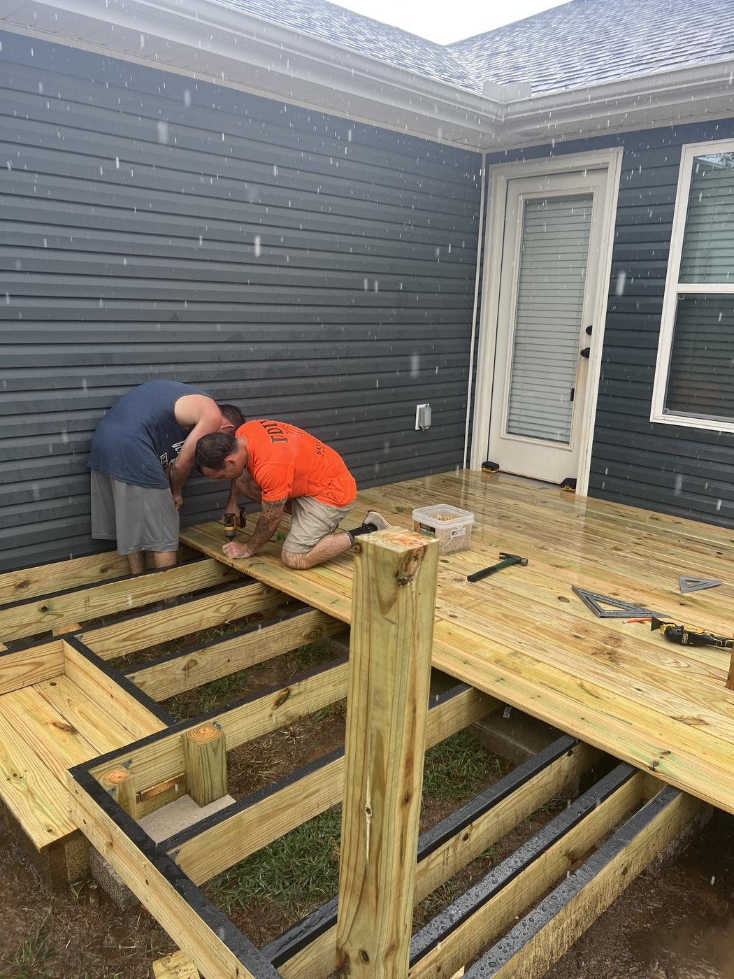 Crew framing a new pressure-treated deck against a blue-sided house