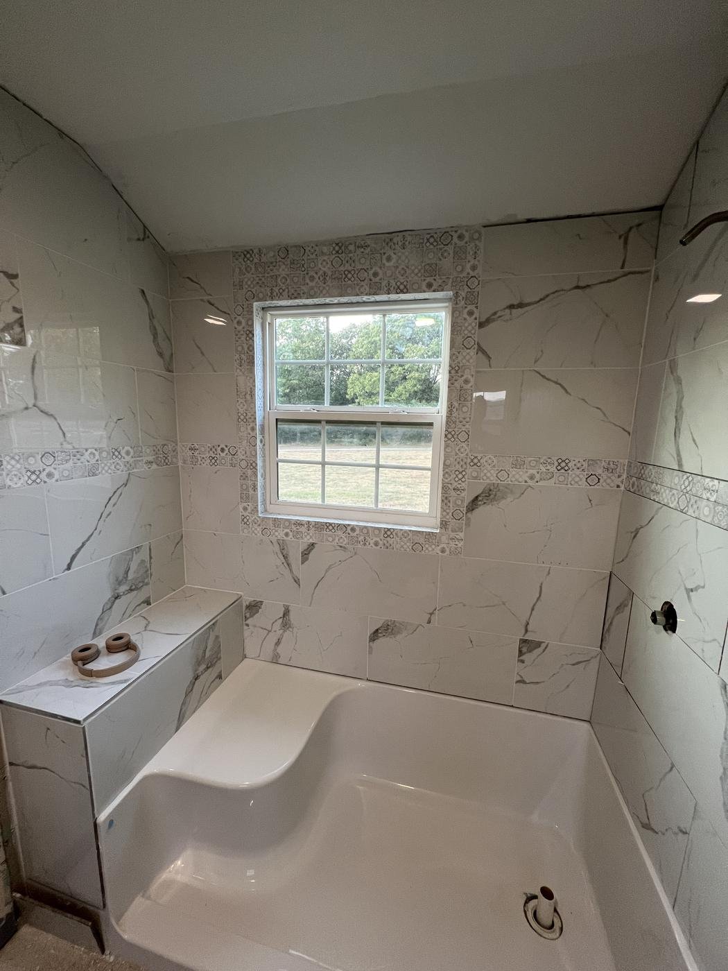 Walk-in shower with marble-look tile and a built-in bench